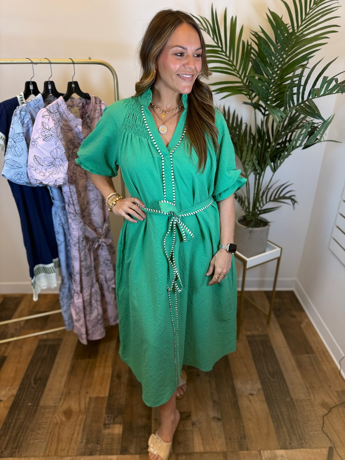 Woman in a green dress standing in a clothing store with racks of dresses in the background.