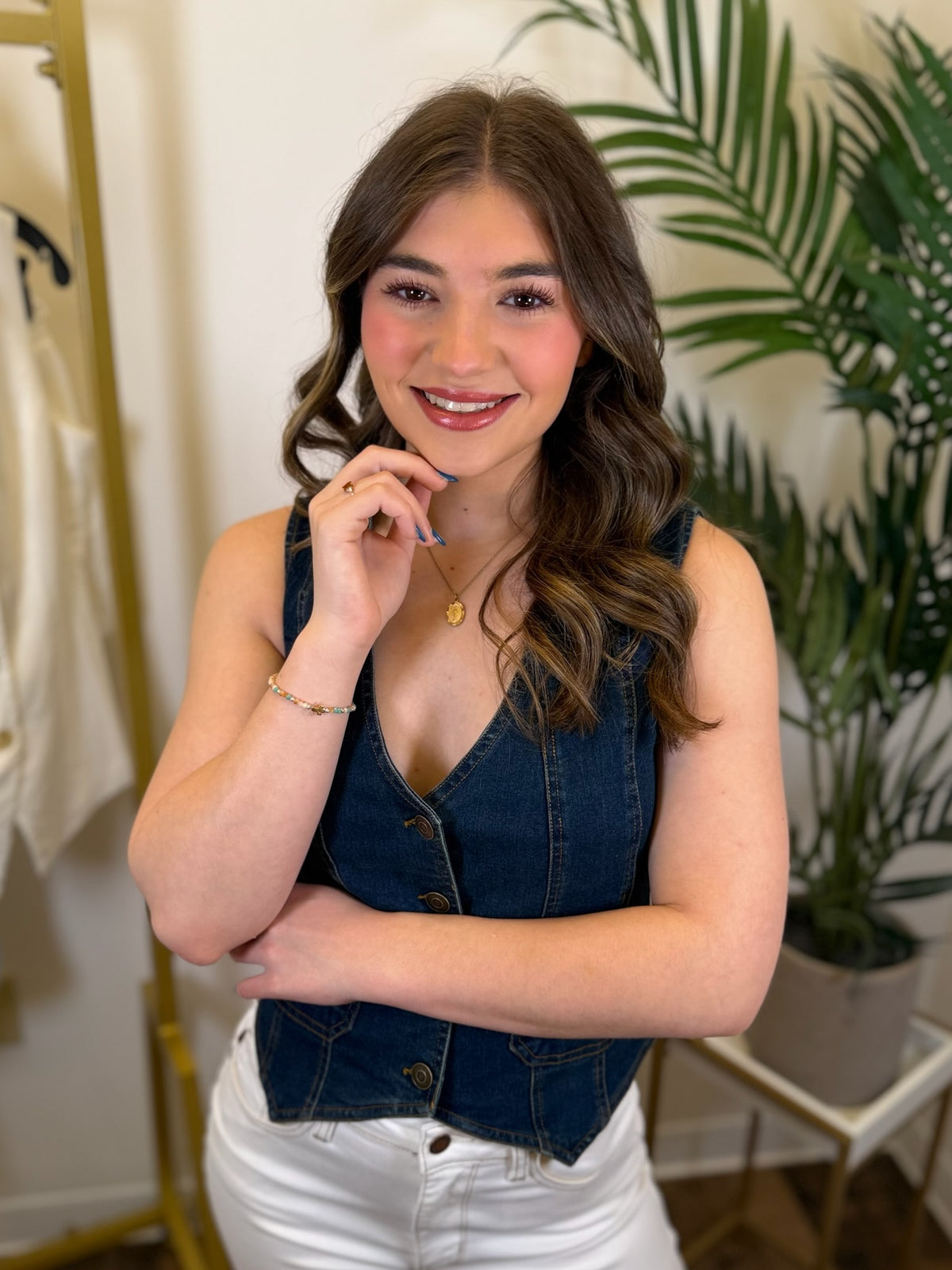 Woman wearing a denim vest and white pants in an indoor setting with plants.