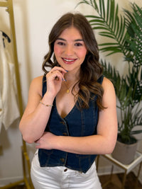 Woman wearing a denim vest and white pants in an indoor setting with plants.