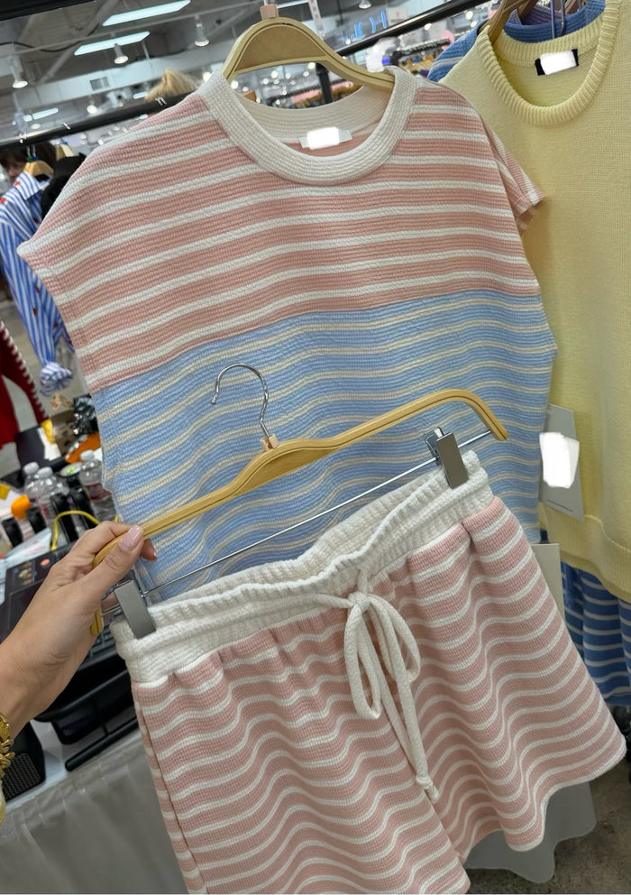 Pink and blue matching striped shirt and shorts set on hangers in a store setting