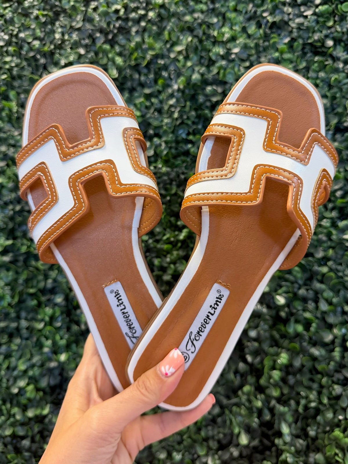 Pair of brown and white flat slide sandals held against a green grass background