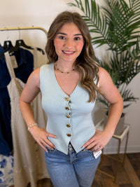 Woman wearing a light sage vest with gold buttons in a clothing store.