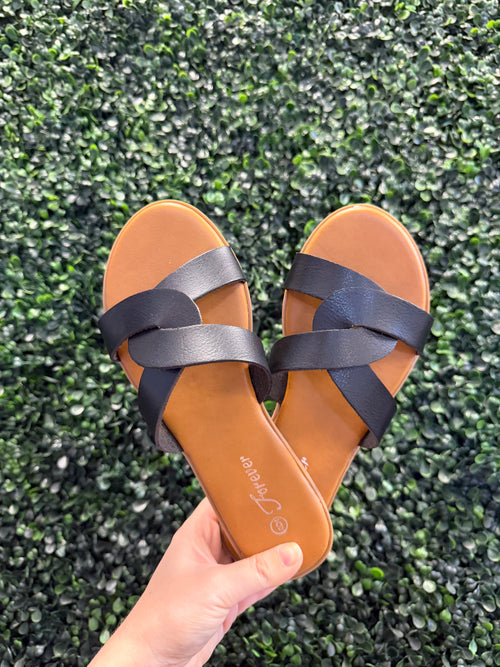 Pair of brown sandals with black straps held against a green grass background