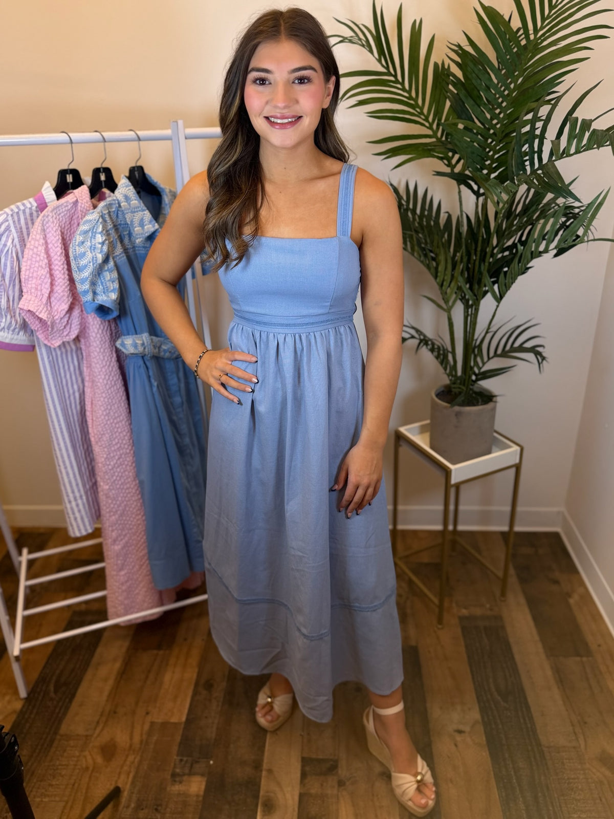Woman wearing a light blue midi dress with square neck in a clothing store setting.