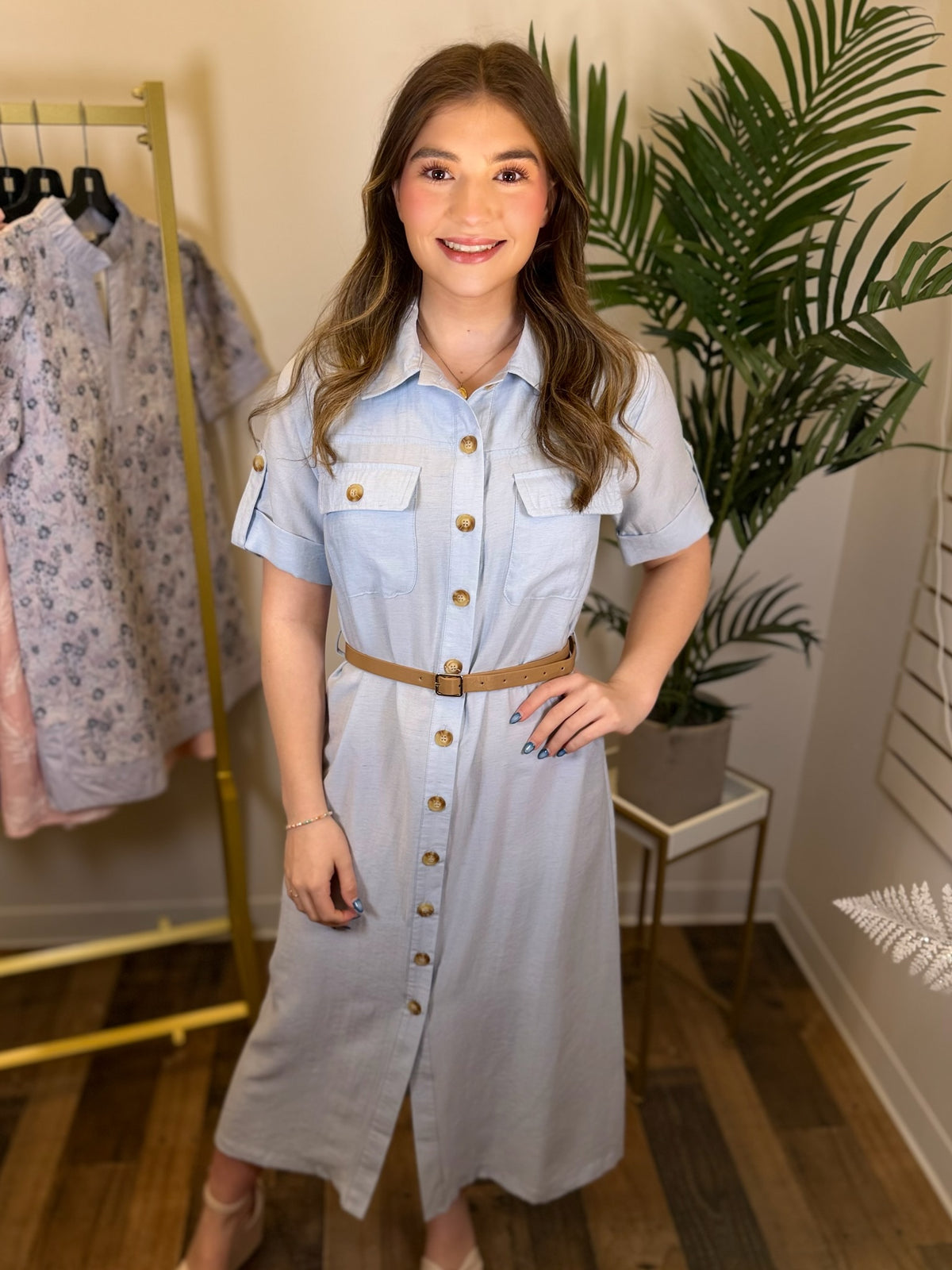 Woman wearing a light blue denim dress with gold buttons in a clothing store.