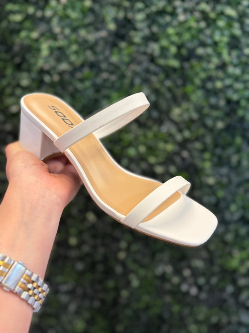 White slip on heel held by a hand with a blurred green background