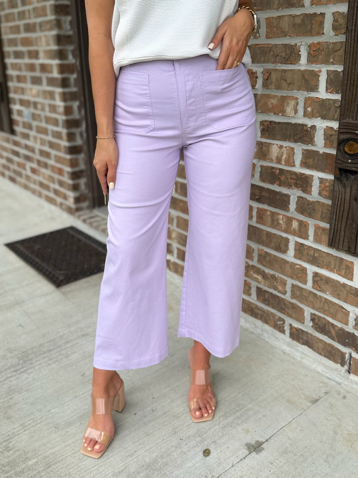 Person wearing light purple pants standing against a brick wall.