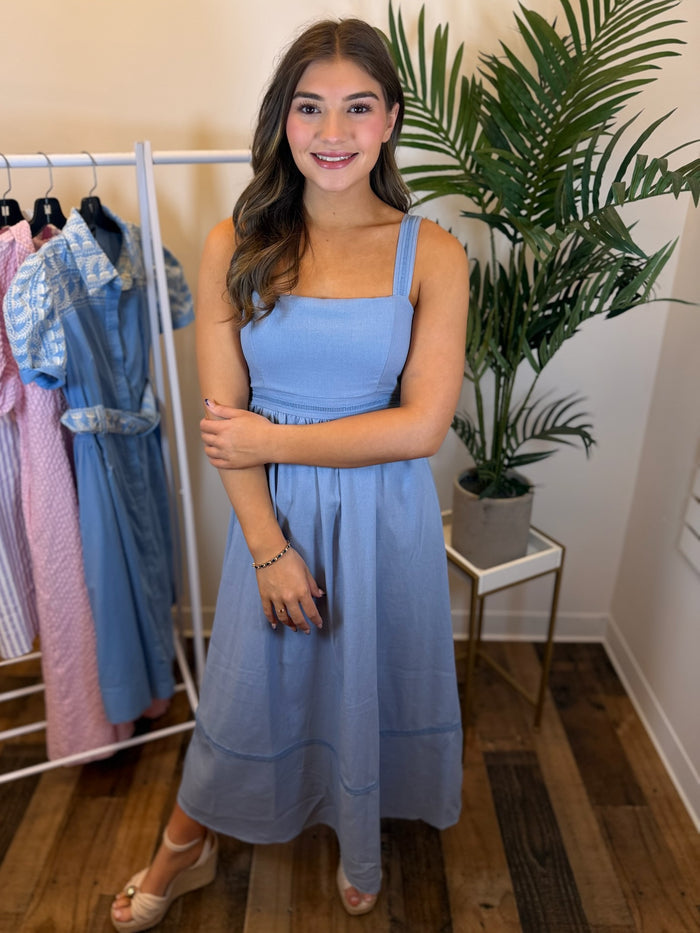 Woman wearing sleeveless blue dress with square neck in a clothing store setting.