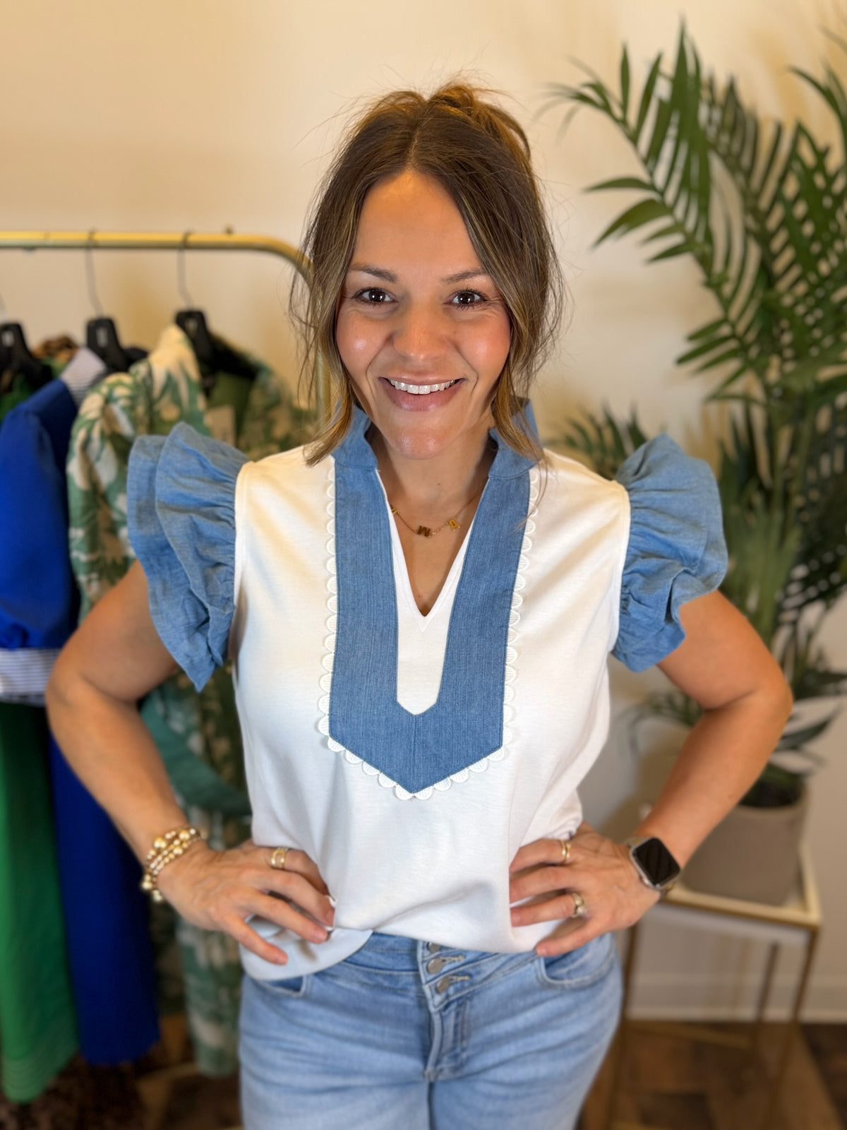 Woman wearing a white blouse with blue accents and jeans, standing in a clothing store.