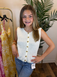 Young girl wearing a white button-up top and blue jeans standing in a clothing store.