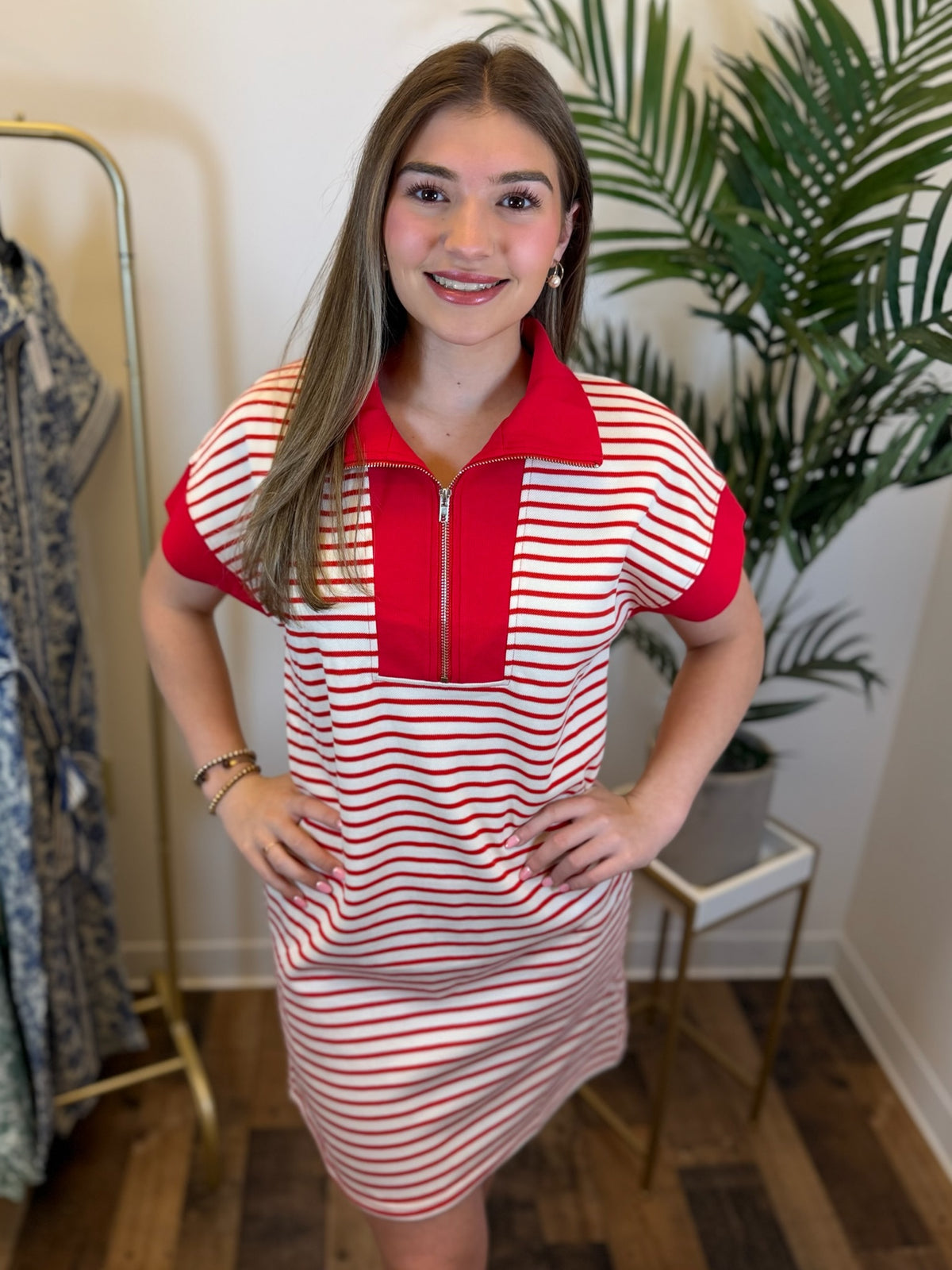 Woman wearing a short sleeve red and white striped dress with quarter zip detail in a room with plants and a mirror.