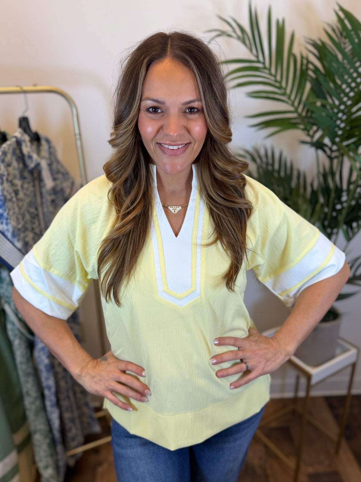 Woman wearing a light yellow blouse with white trim in a clothing store.