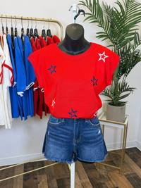 Red cap sleeve top with navy and white star patterns on a mannequin in a clothing store setting.