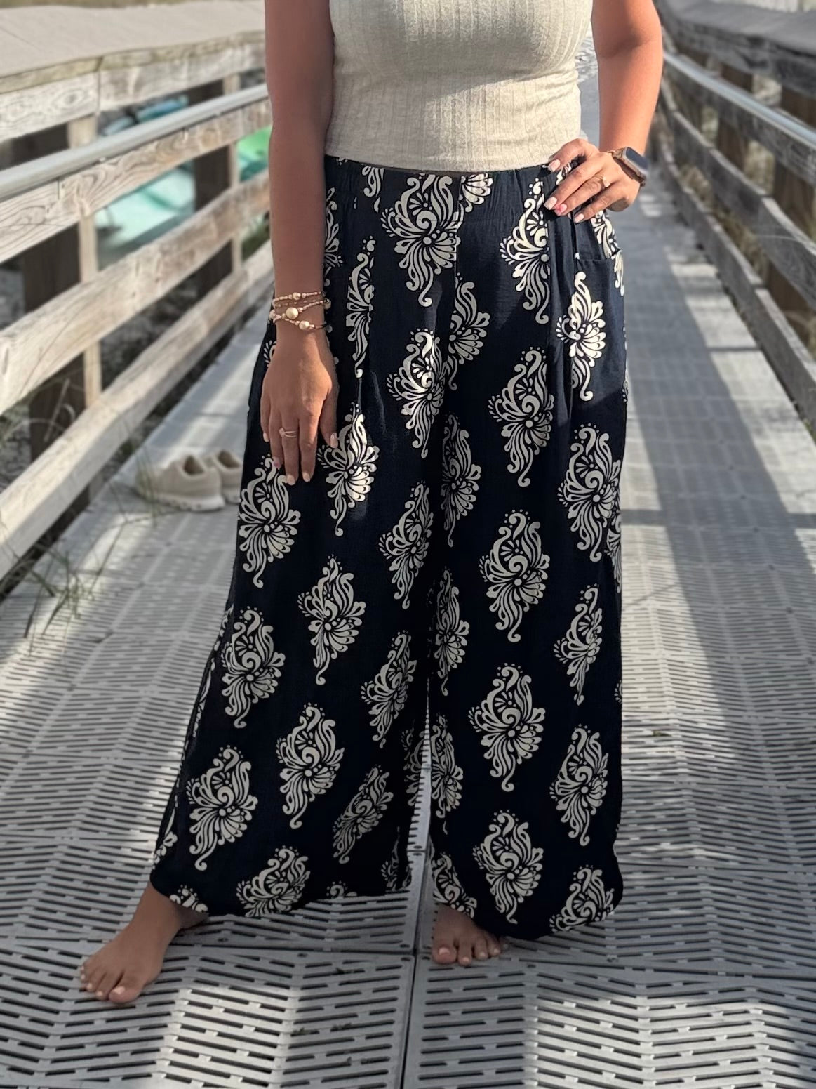 Person wearing navy patterned pants with a wide, flowy fit and elastic waistband standing on a wooden deck.