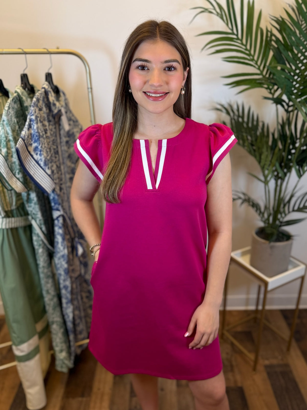 Woman wearing short fuchsia dress with v neck and ruffled cap sleeves standing in a clothing store setting.