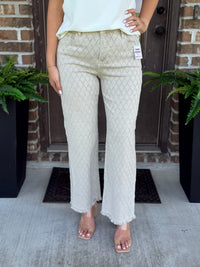 A person wearing light beige textured straight leg pants with a frayed hem, paired with a white top and clear high-heeled sandals, standing on a concrete porch in front of a brick door.