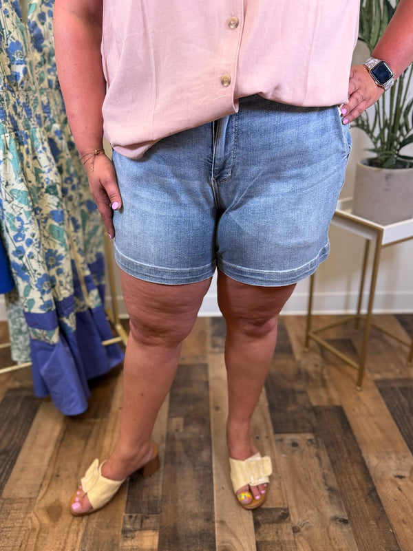 Person wearing a pink shirt and light blue high rise denim shorts standing on a wooden floor.