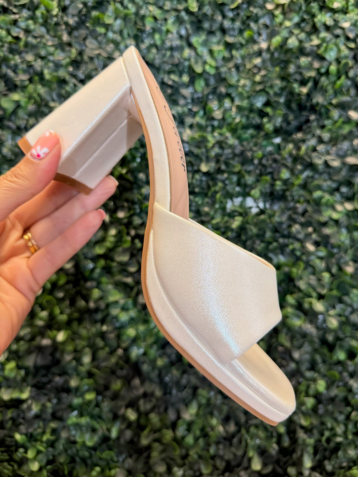 White block heel with open toe being held against a textured green background