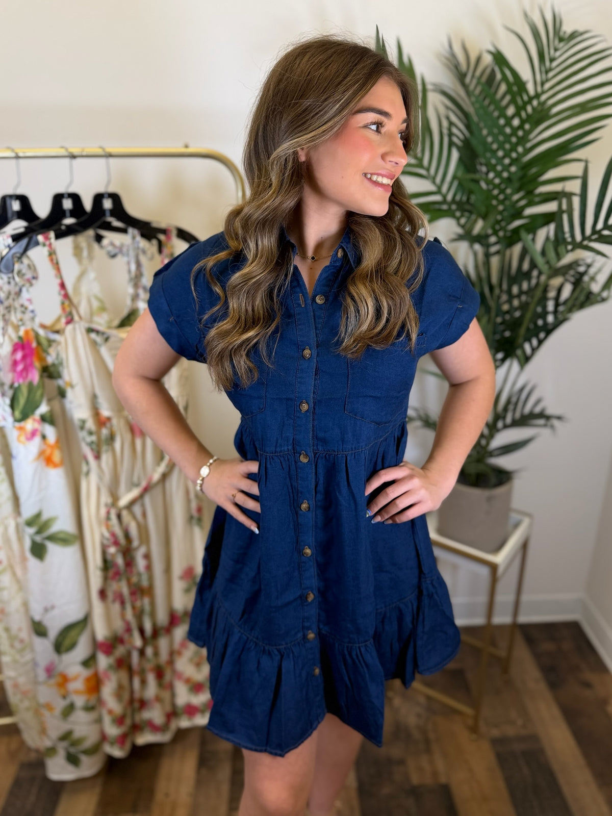 Woman wearing a blue dress standing in a clothing store with plants in the background