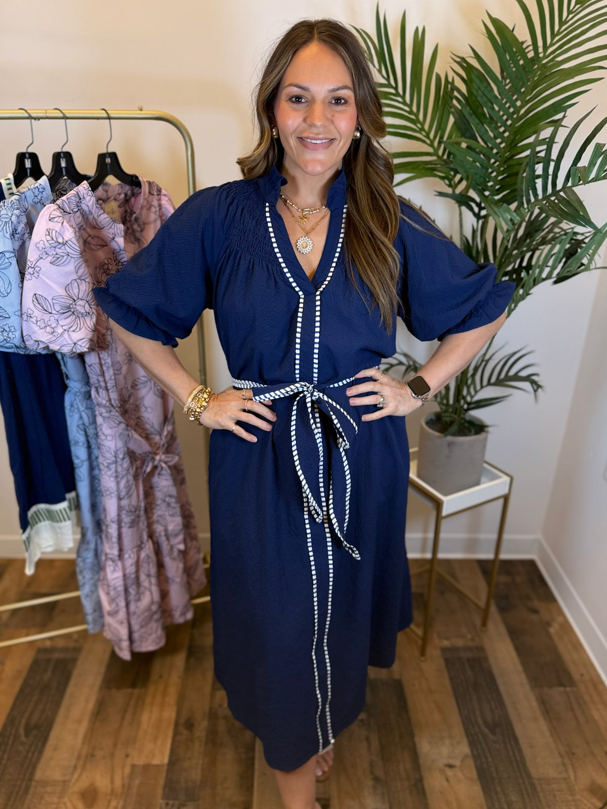 Woman wearing a navy dress with white trim and puff sleeves in a clothing store.