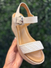 Beige sandal with a strap held against a blurred green background