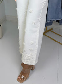 Cream pants with 3d floral embroidery worn by a person on a white floor.