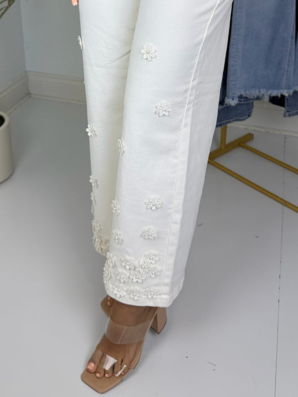 Cream pants with 3d floral embroidery worn by a person on a white floor.