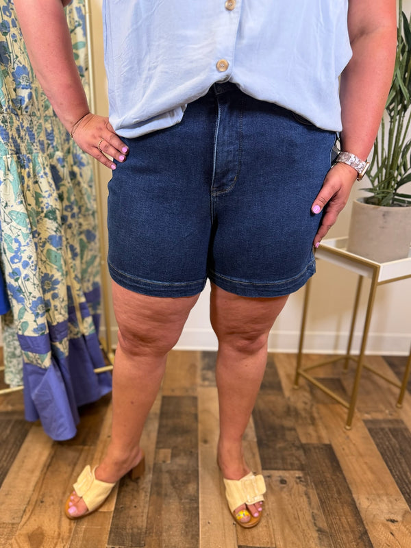 Person wearing dark blue denim shorts and a light blue shirt in an indoor setting.