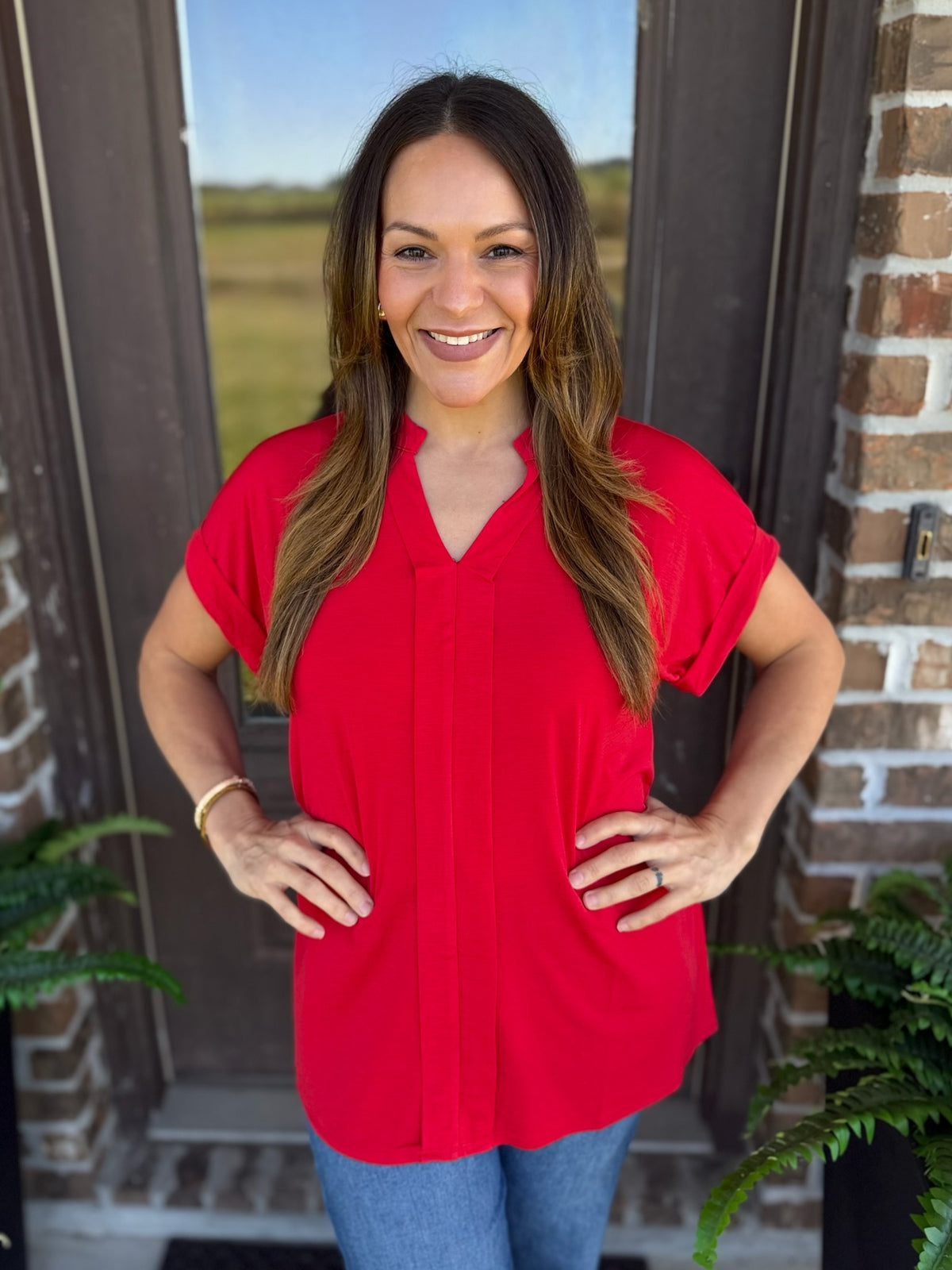 Woman wearing a red short sleeve blouse with a split V-neckline, standing outdoors.