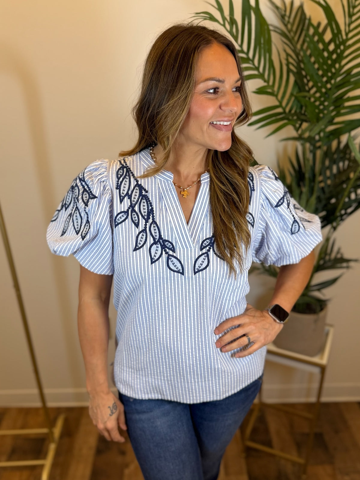 Woman wearing a blue and white striped blouse with embroidery and split neckline, standing indoors.