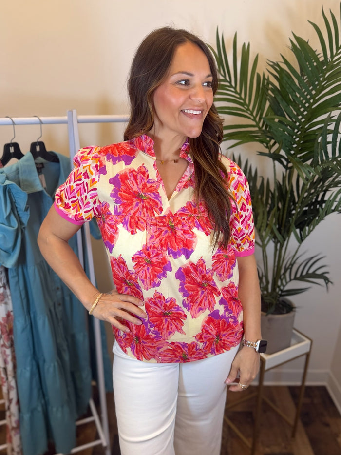Woman wearing a colorful floral blouse with contrast short sleeves in a clothing store.