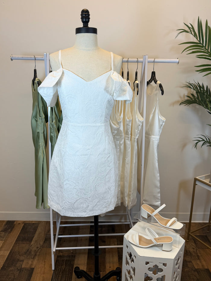 White textured mini dress on a mannequin with shoes and greenery in the background