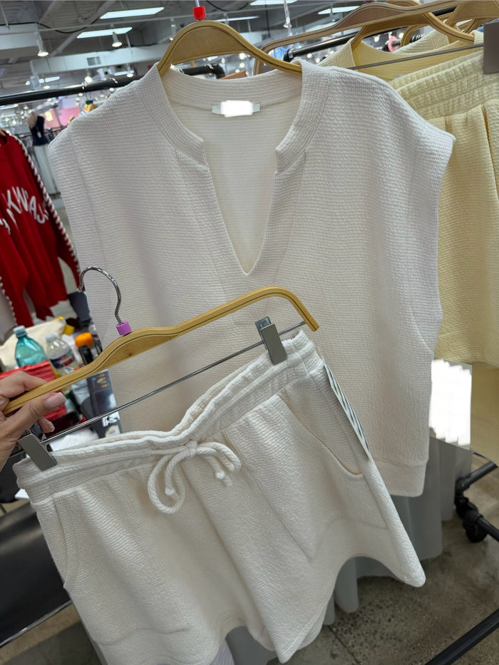 White textured split neck top and elastic waist shorts on hangers in a store setting
