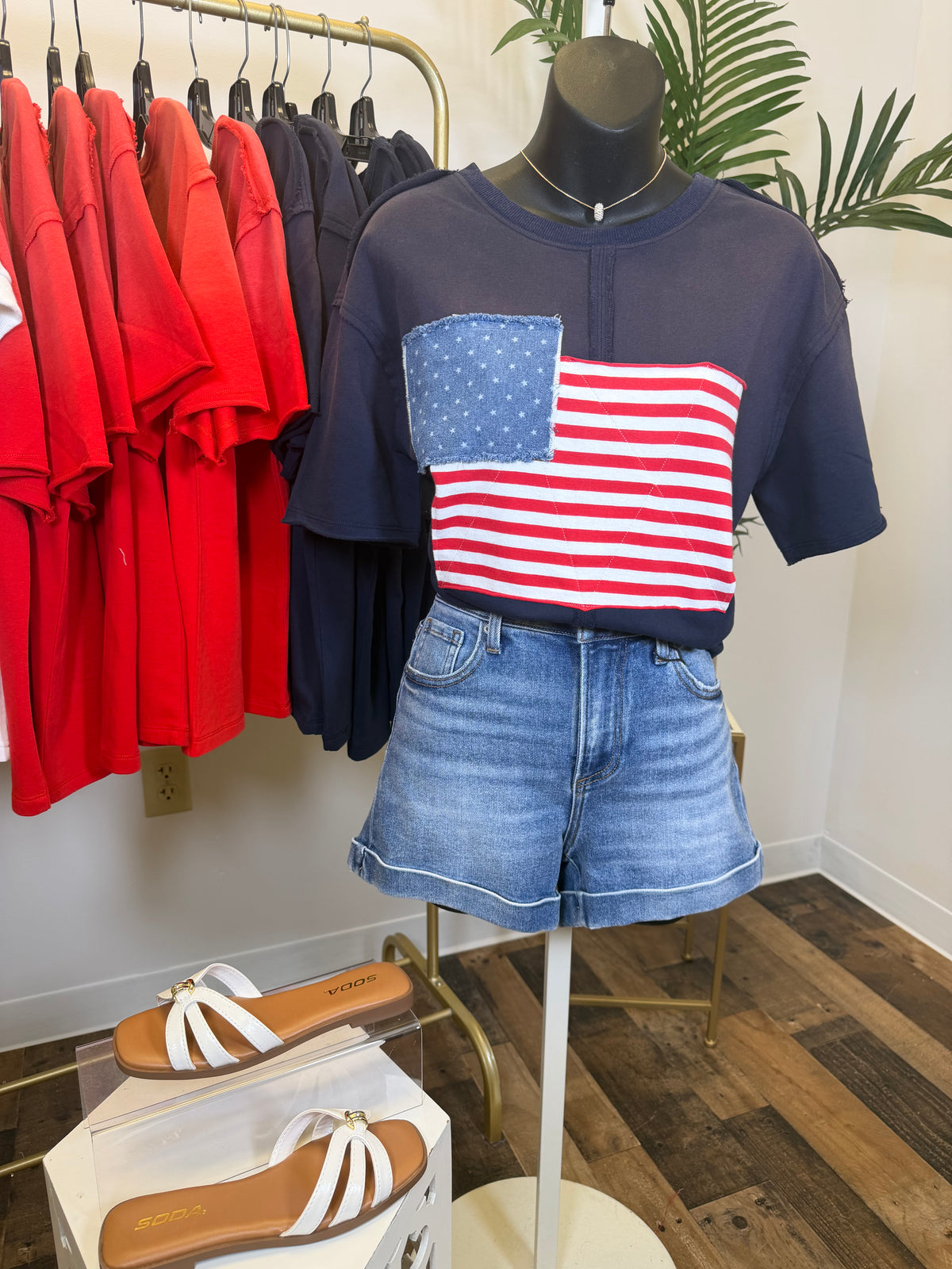 Navy blue vintage wash t-shirt with American flag design on a mannequin, surrounded by colorful shirts on hangers.