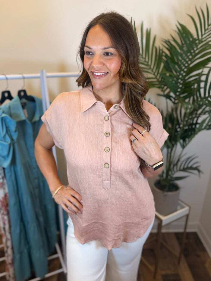 Woman wearing light pink woven top with button details and collar.