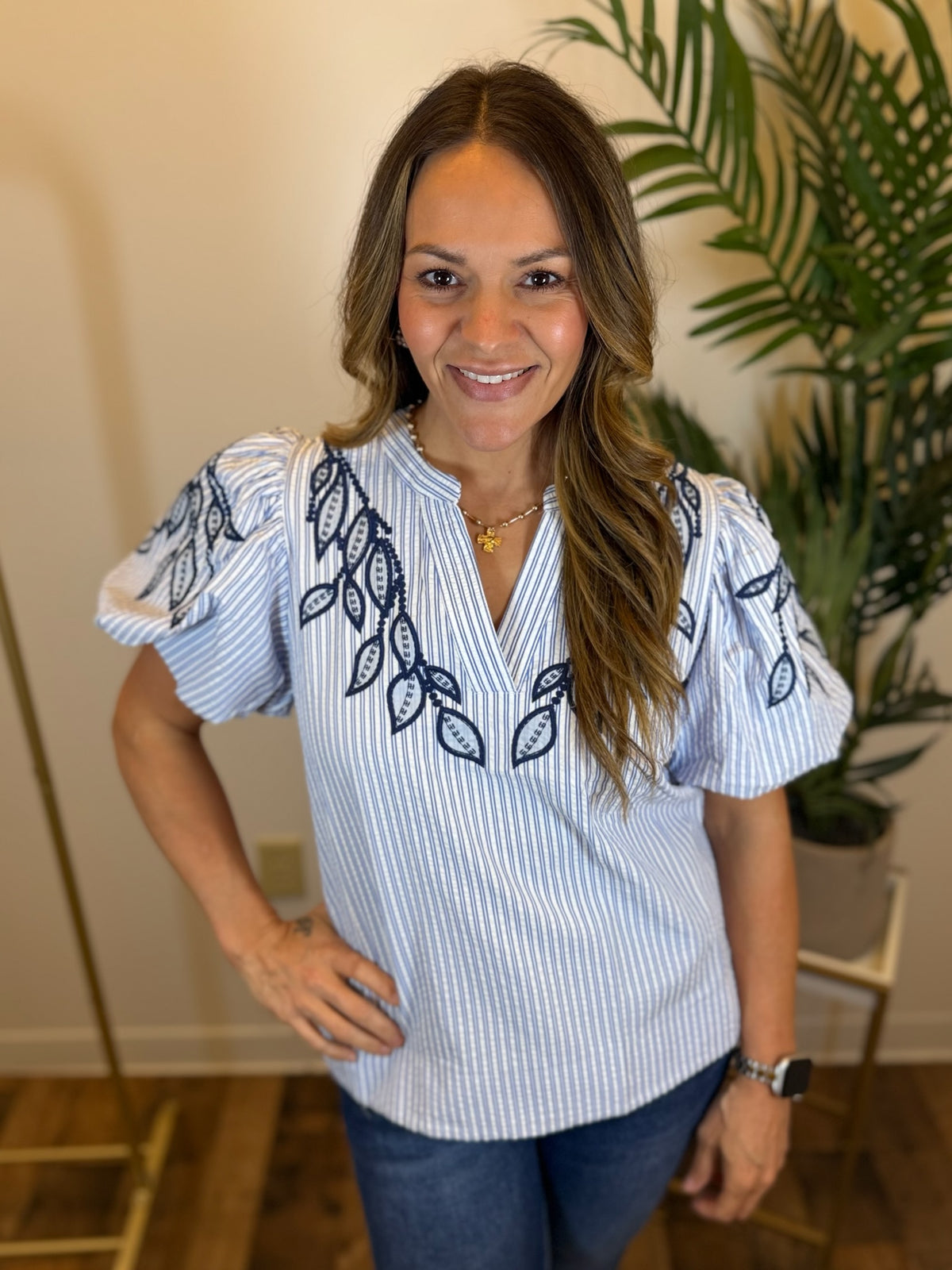 Woman wearing a white blouse with blue embroidery in a room with a plant