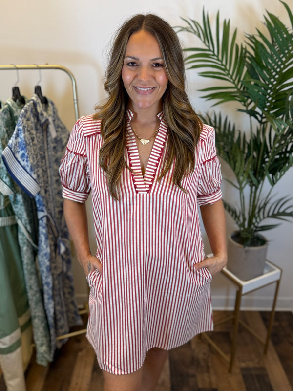 Woman wearing a red and white striped dress with red trim details and short puff sleeves in a clothing store.