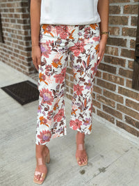 Person wearing cream wide leg pants with pink, orange, and purple floral accents standing against a brick wall.