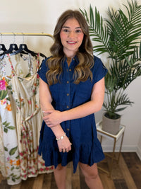 Woman wearing a blue dress standing in a clothing store with plants in the background