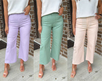 Three women wearing different colored pants against a brick wall.