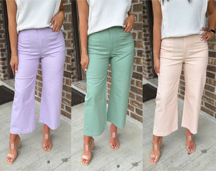 Three women wearing different colored pants against a brick wall.