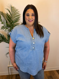 Woman wearing a blue denim shirt with buttons indoors next to a plant