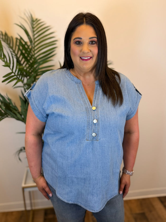 Woman wearing a blue denim shirt with buttons indoors next to a plant