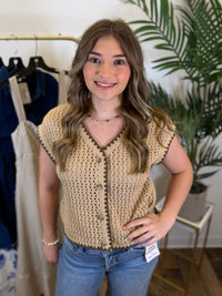 Woman wearing a beige short sleeve crochet top with contrast trim and blue jeans in a clothing store.