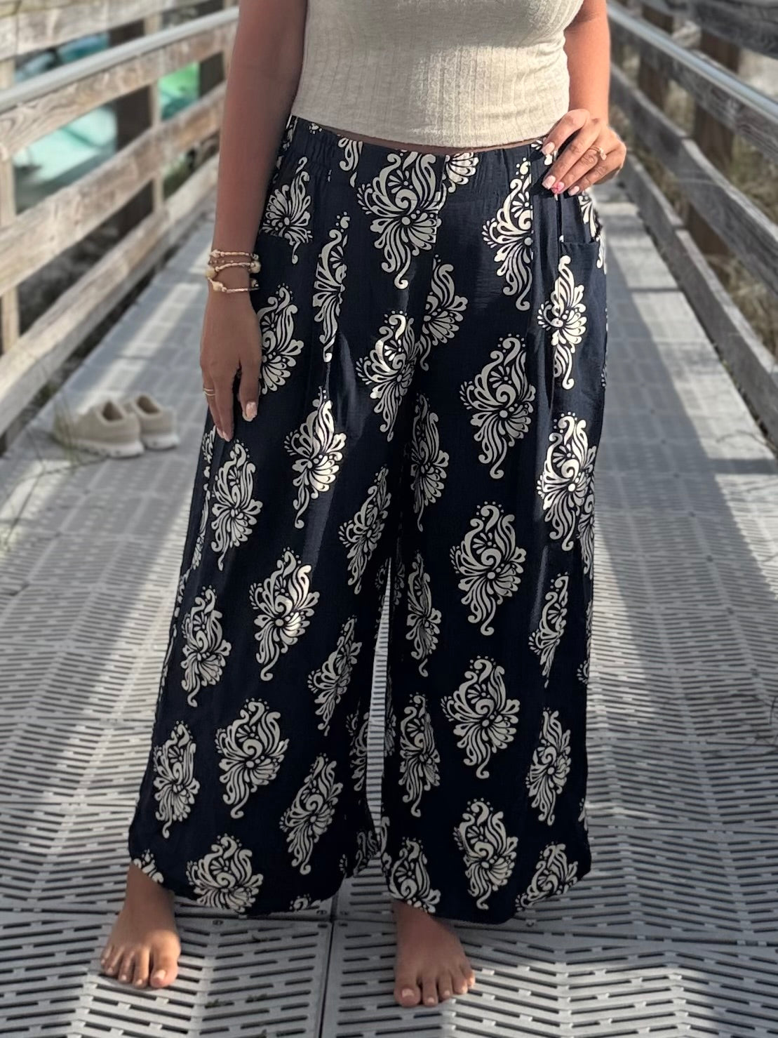 Person wearing navy blue wide-leg pants with white floral patterns and an elastic waist on a wooden deck.