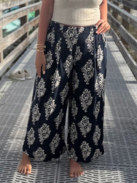Person wearing navy blue wide-leg pants with white floral patterns and an elastic waist on a wooden deck.