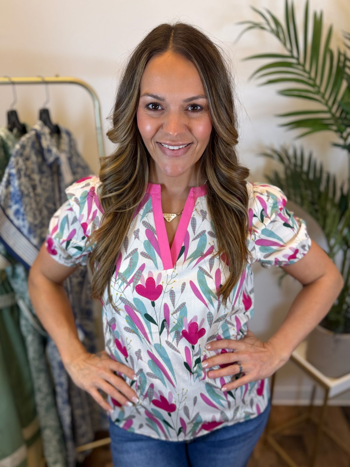 Woman wearing a colorful floral blouse with pink neckline accents and short puff sleeves in a clothing store.