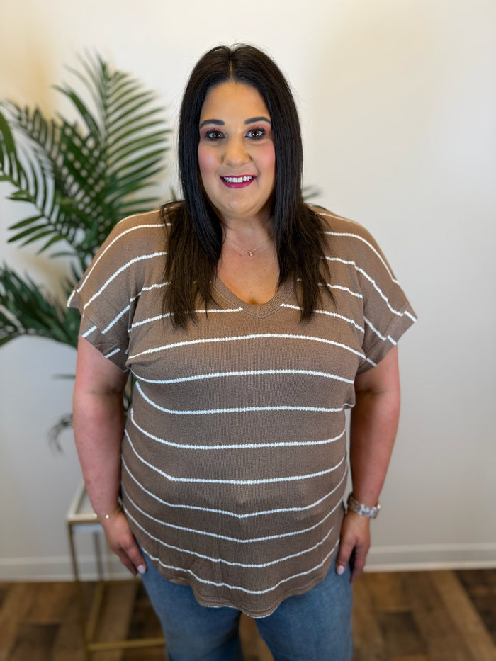 Woman wearing a brown and white striped shirt in an indoor setting with a plant in the background