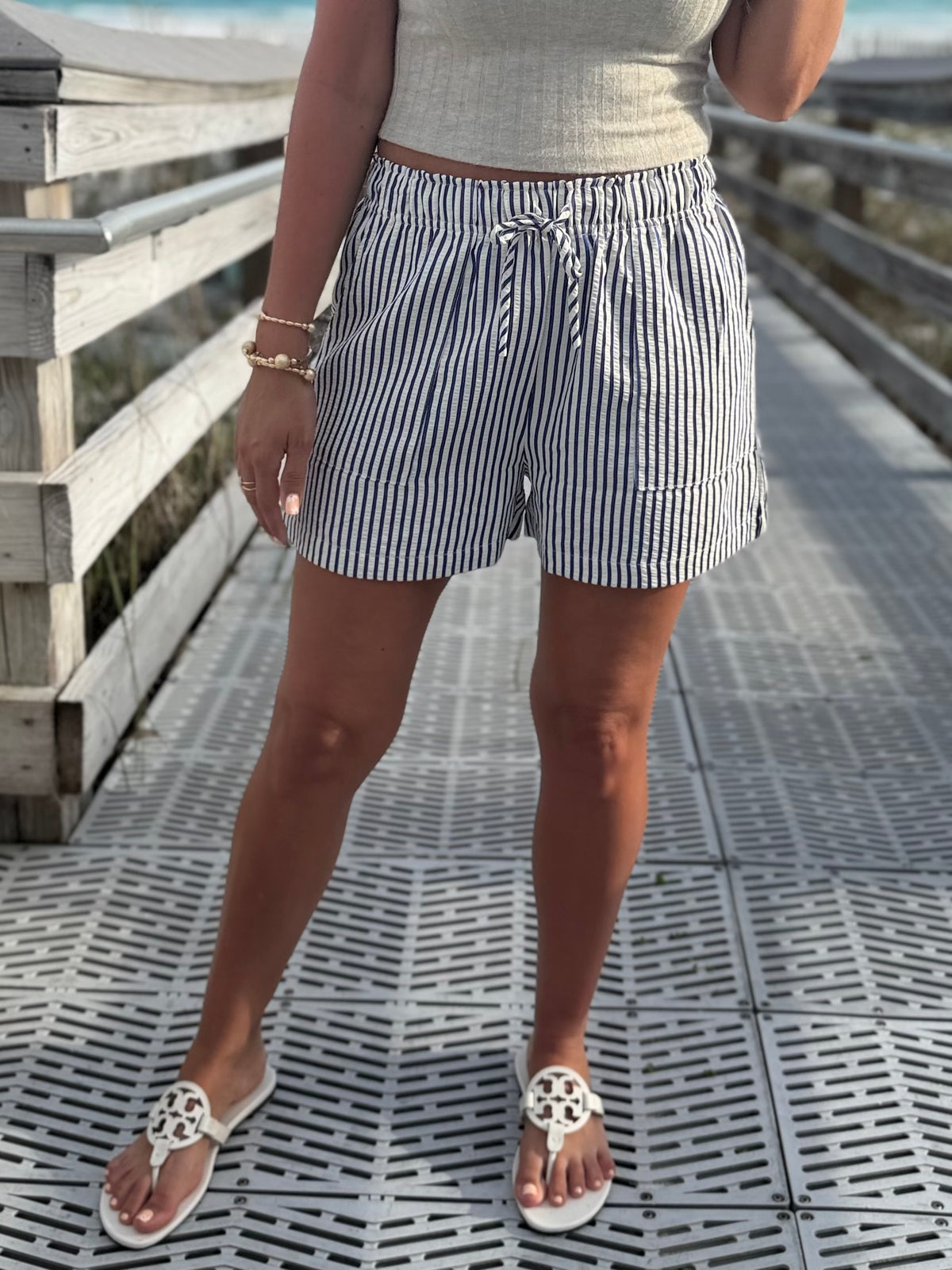 Person wearing striped shorts with elastic waistband and sandals on a wooden deck.