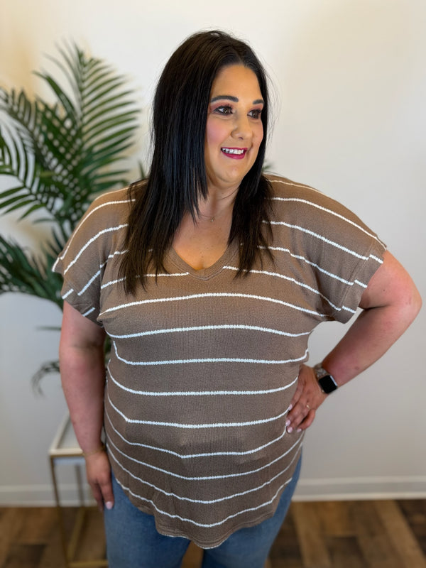 Woman wearing a brown and beige striped shirt indoors with a plant in the background